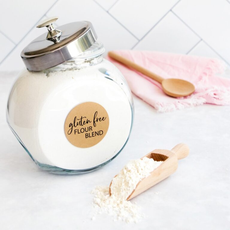 A large jar of flour on a grey background, with a small wooden scoop of flour in front. Jar label reads: "gluten free flour blend".