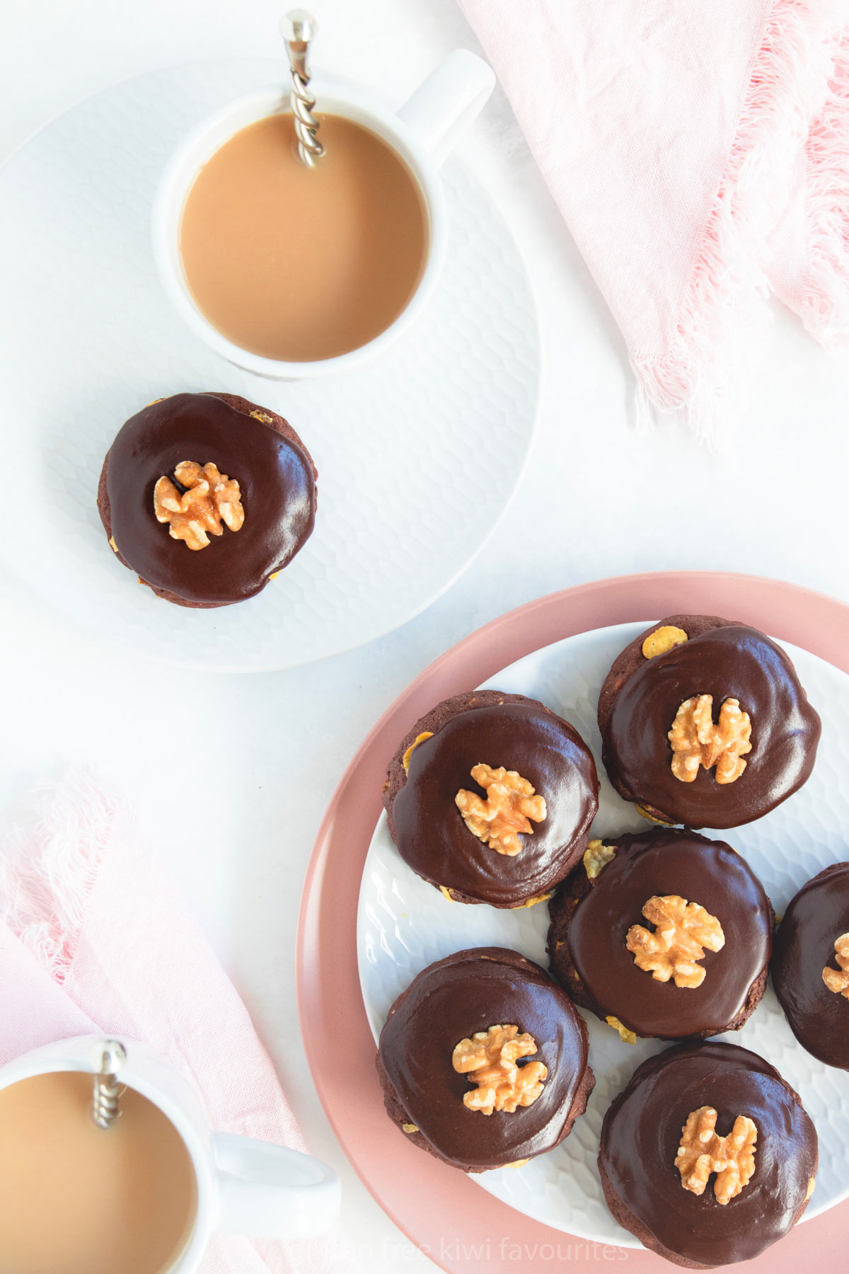 Top view of a pink plate of afghan biscuits and two cups of tea in grey mugs.