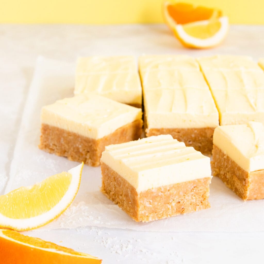 Square pieces of gluten free citrus slice on a yellow background with slices of lemon and orange.