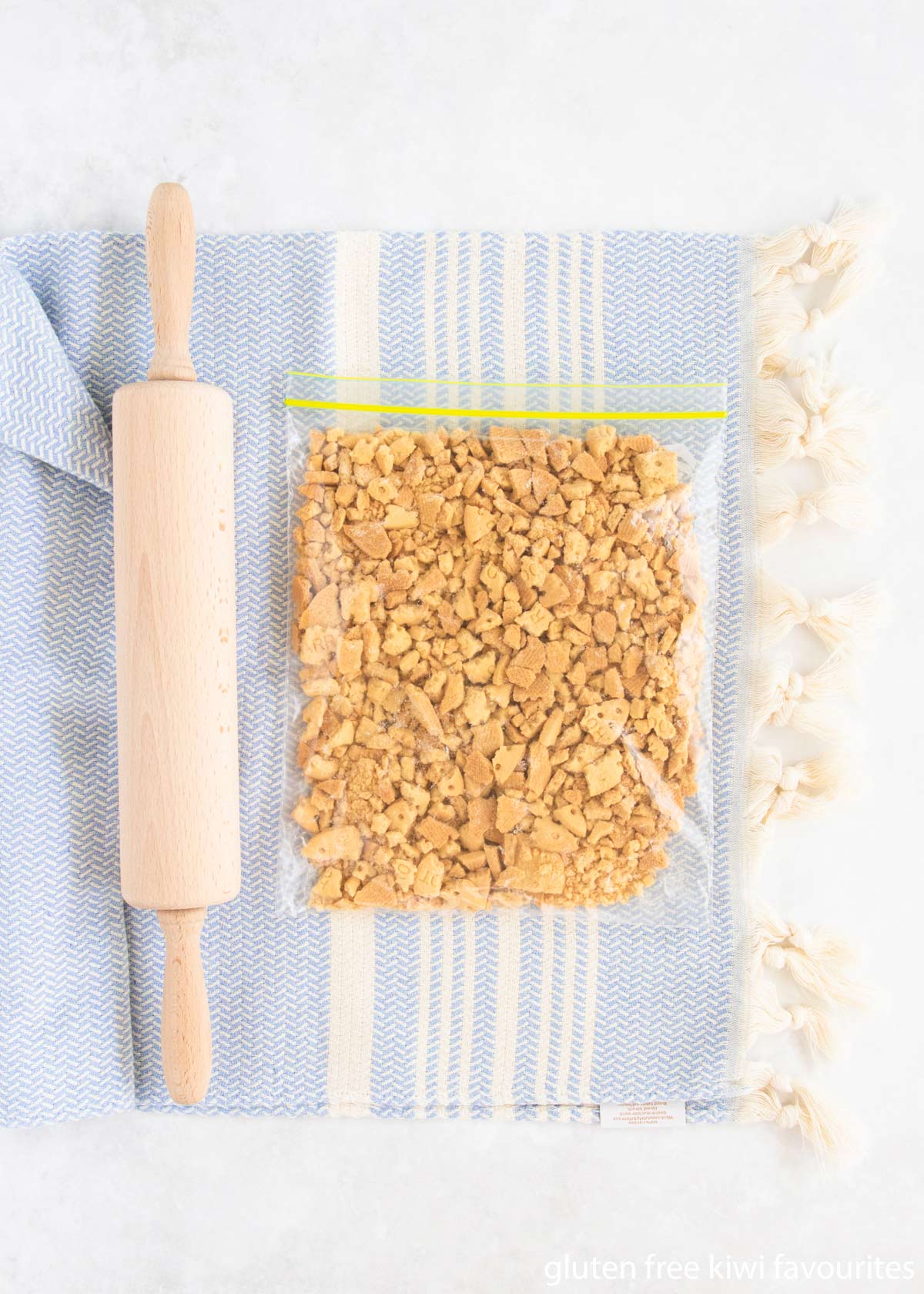 Gluten free arrowroot biscuits being crushed in a plastic bag with a rolling pin.