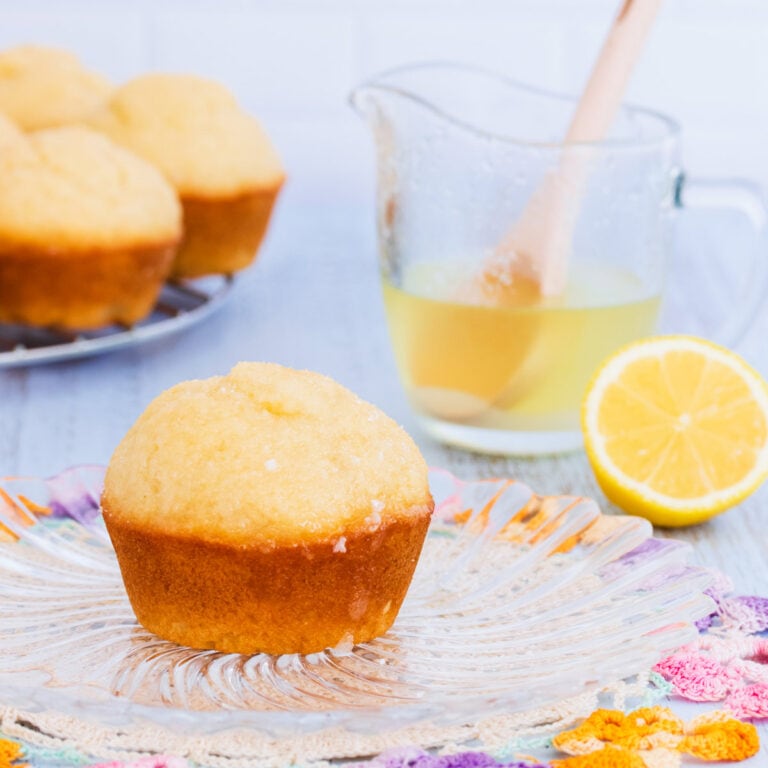 A gluten free lemon muffin on a glass plate, with a blue background.