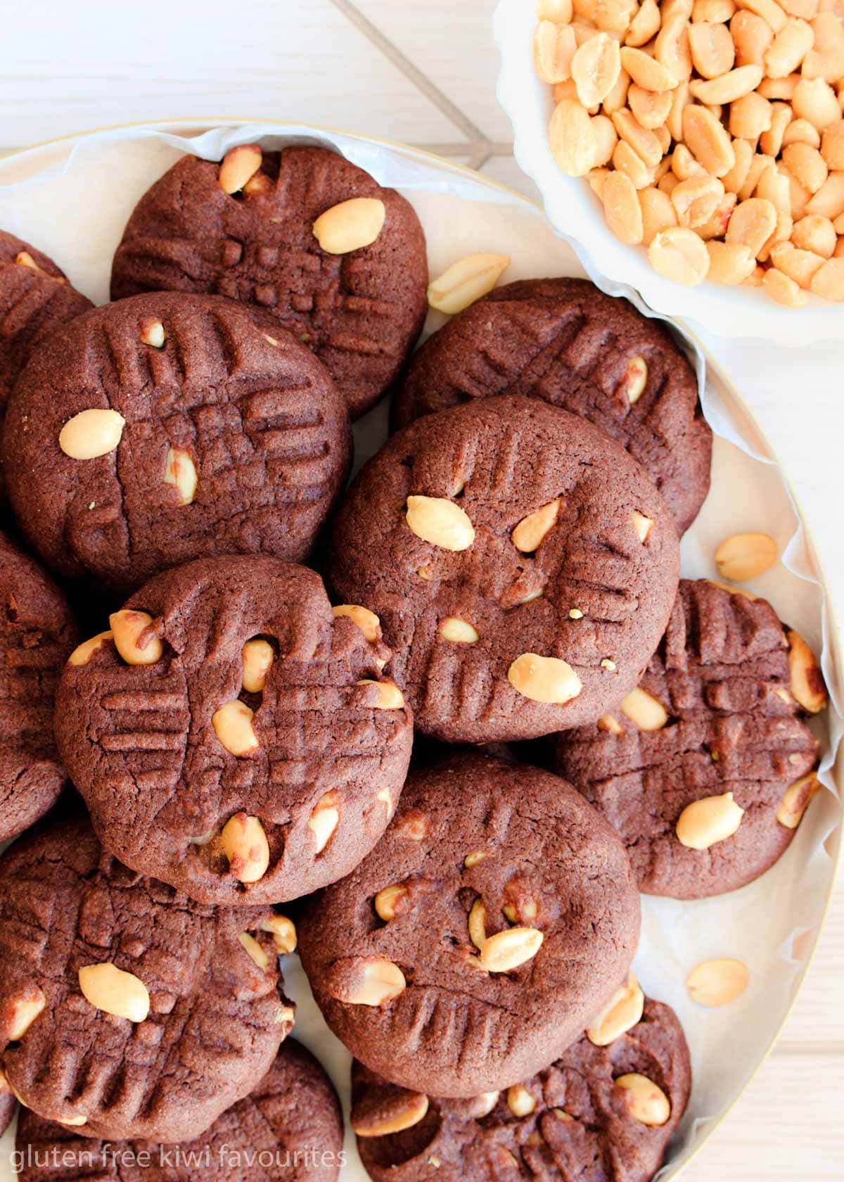 Gluten free peanut brownie biscuits piled on a round plate with a small bowl of peanuts.