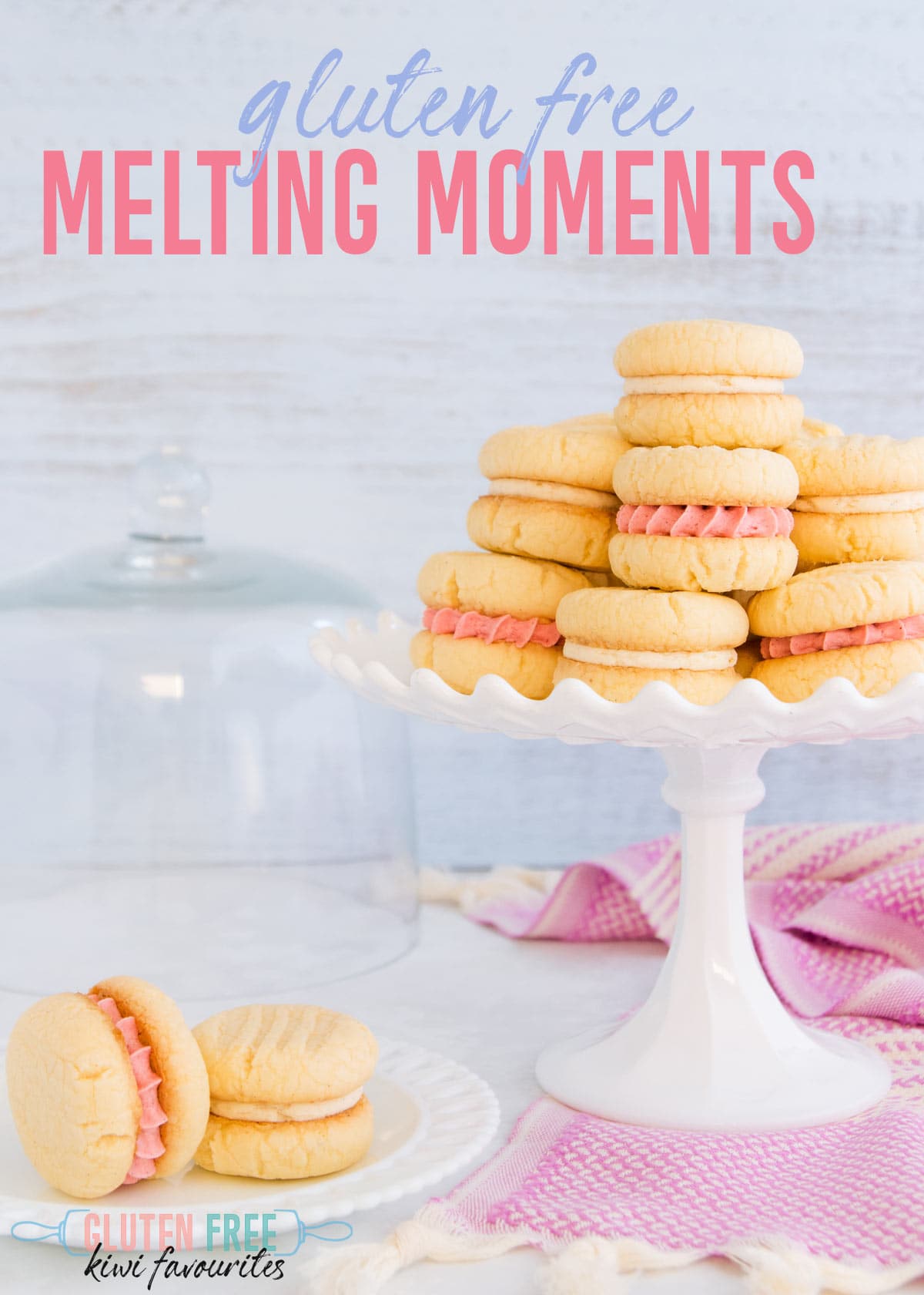 Biscuits filled with pink and white buttercream on a white milk glass cake stand on a pale blue background, text overlay reads "gluten free melting moments"