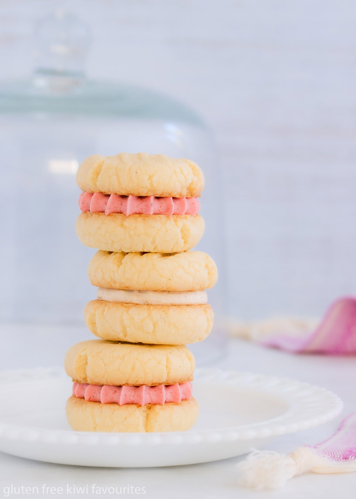 A stack of three melting moments, two with strawberry buttercream and one with vanilla, on a white glass plate.