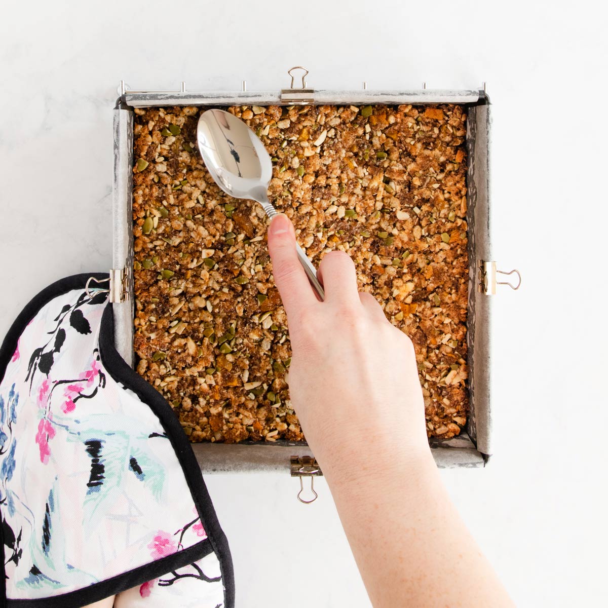 The freshly baked muesli bar being pressed down with the back of a spoon.