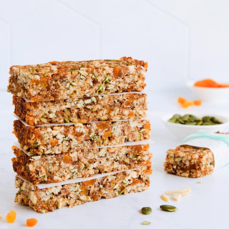 A stack of five gluten free muesli bars on a pale grey background, with scattered nuts and seeds.