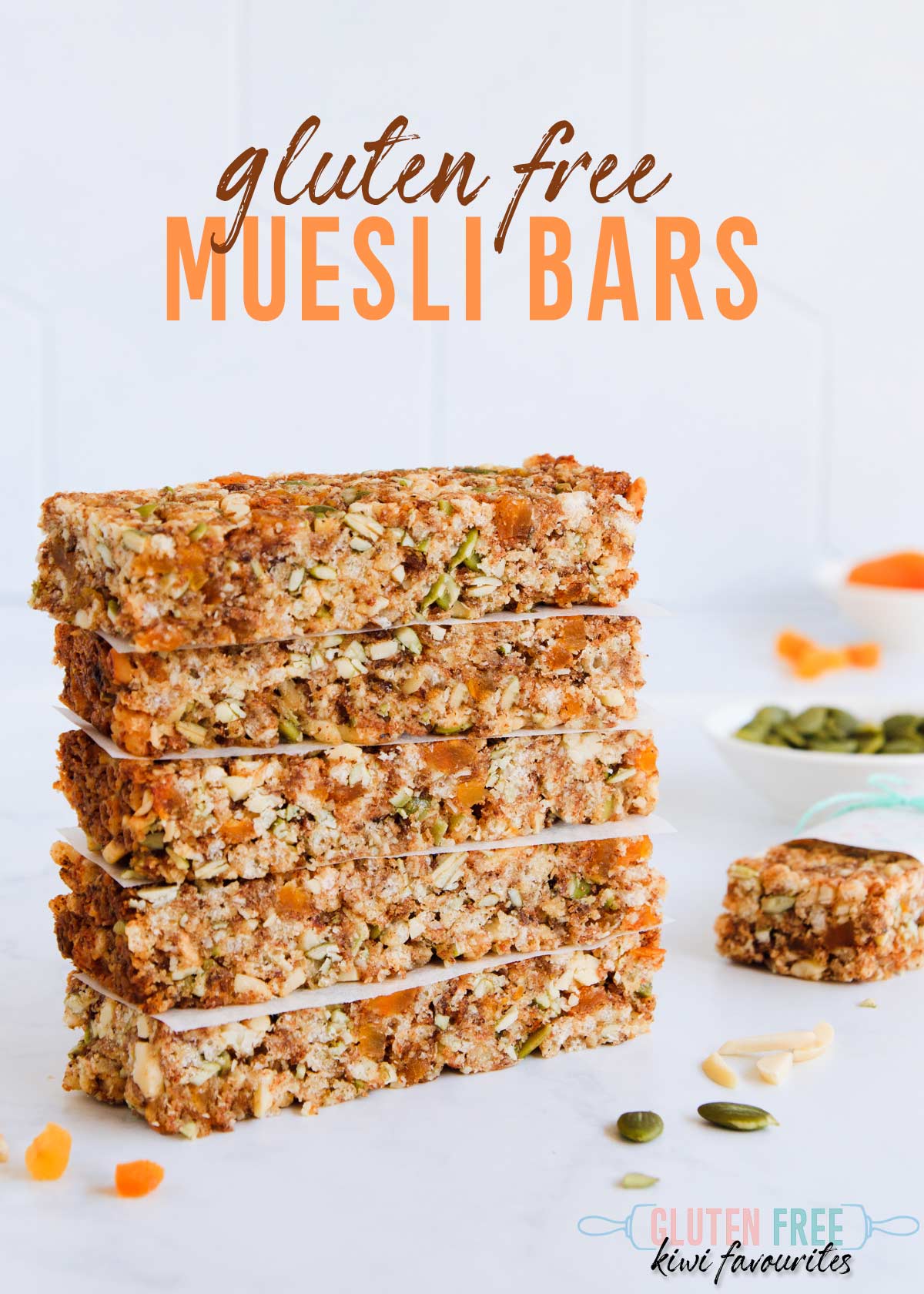 Five stacked muesli bars on a grey background, with scattered almonds and pumpkin seeds, text overlay reads "gluten free muesli bars".