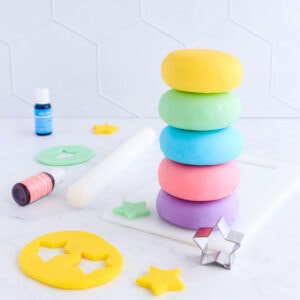 Five stacked balls of playdough - yellow, green, blue, pink and purple on a grey background, with yellow play dough star cutouts and a star cutter.