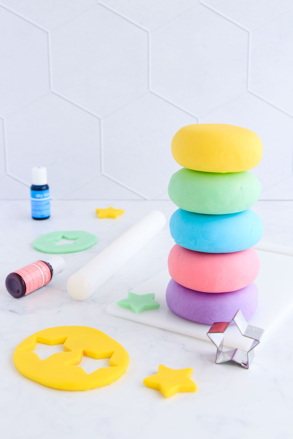 Five stacked balls of playdough - yellow, green, blue, pink and purple on a grey background, with yellow play dough star cutouts and a star cutter.