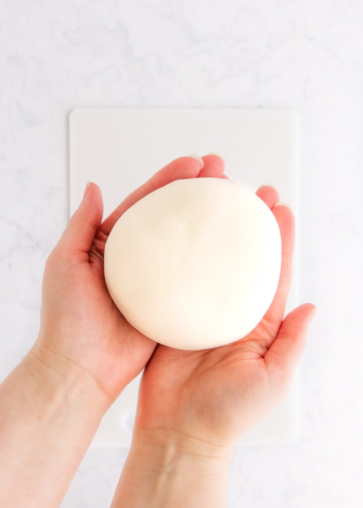 A smooth ball of white gluten free playdough being held in two hands.