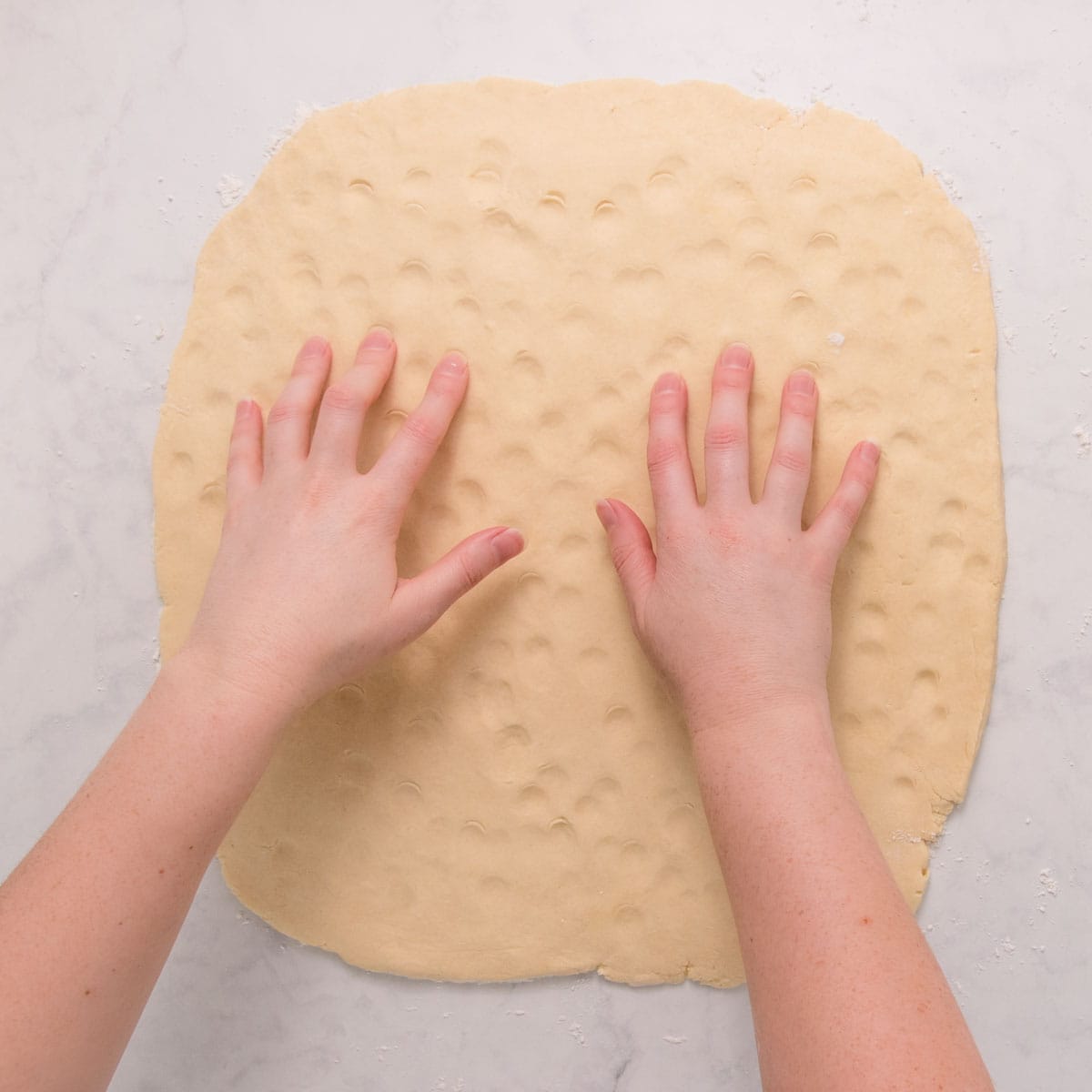 Hands lightly pressing the surface of the dough to create dimples all over.