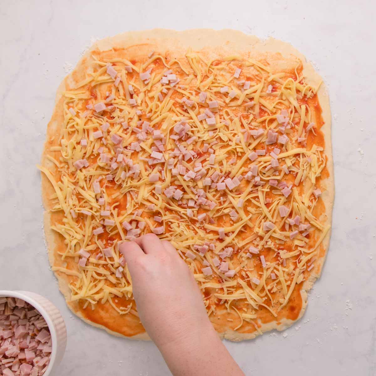 Spreading grated cheese and chopped ham over the surface of the dough.