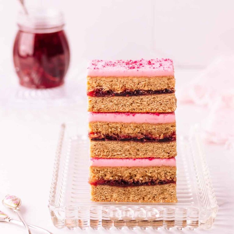 Three stacked pieces of Belgian slice on a rectangular glass plate, with a small jar of raspberry jam in the background.