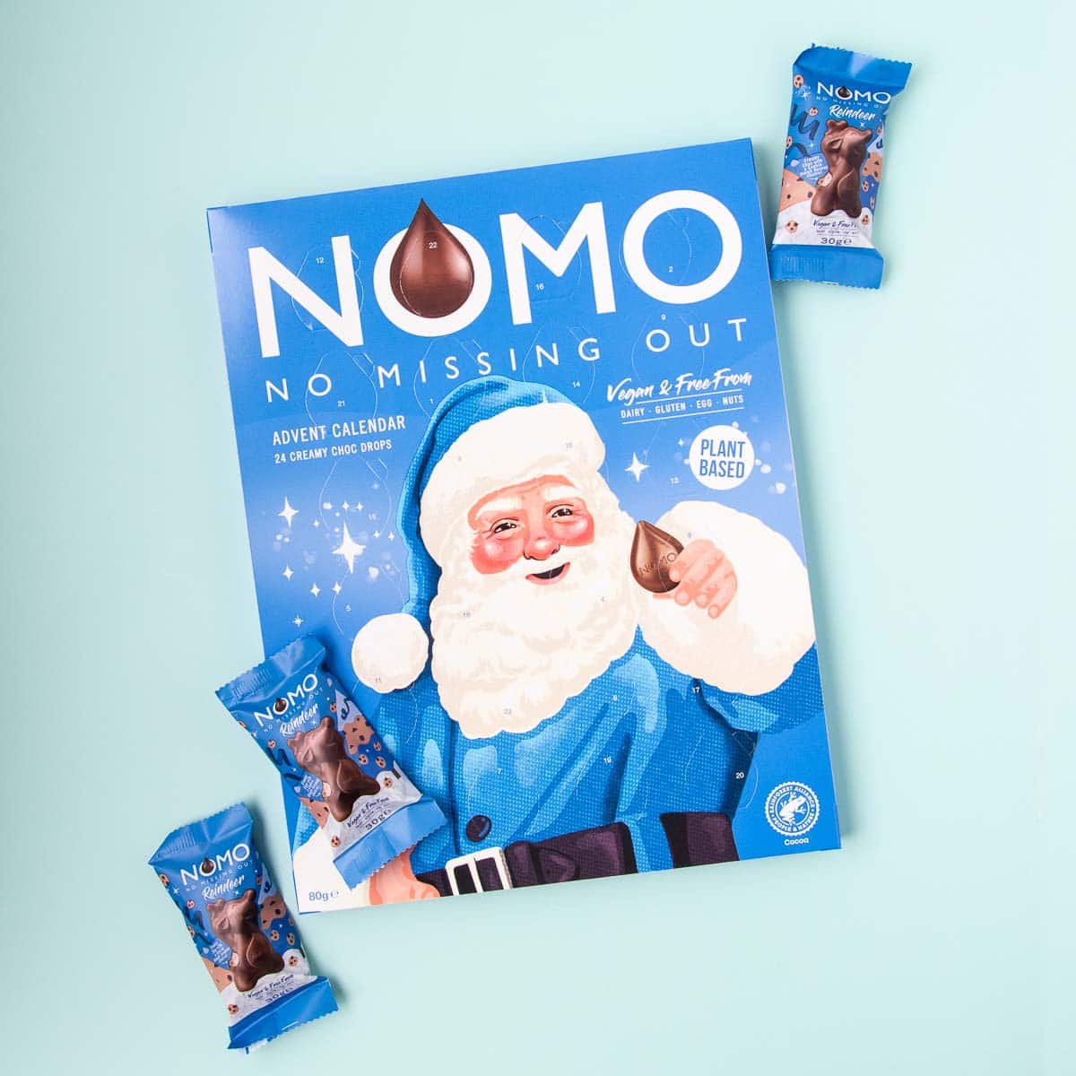A blue NOMO brand advent calendar with three NOMO chocolate reindeer, on a mint green background.