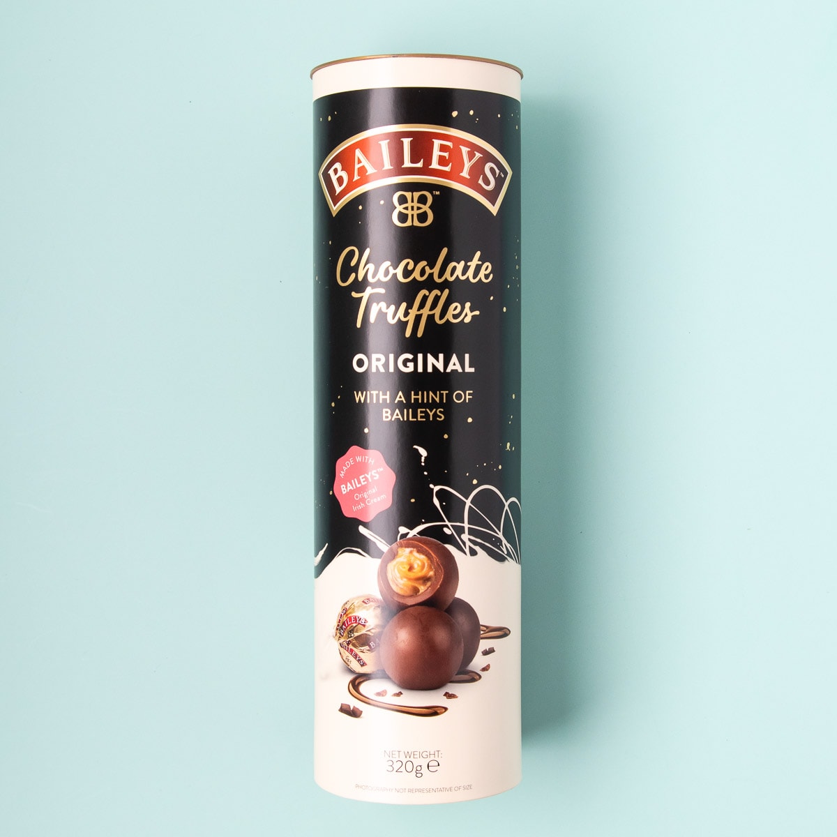 A tall tube-shaped container of Baileys chocolate truffles, on a mint green background.
