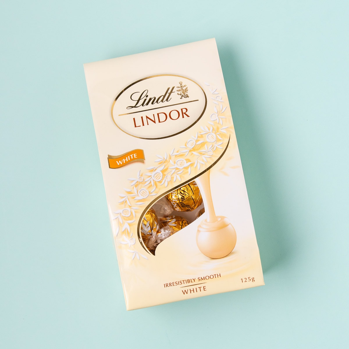 A bag of Lindt white chocolate truffles, on a mint green background.