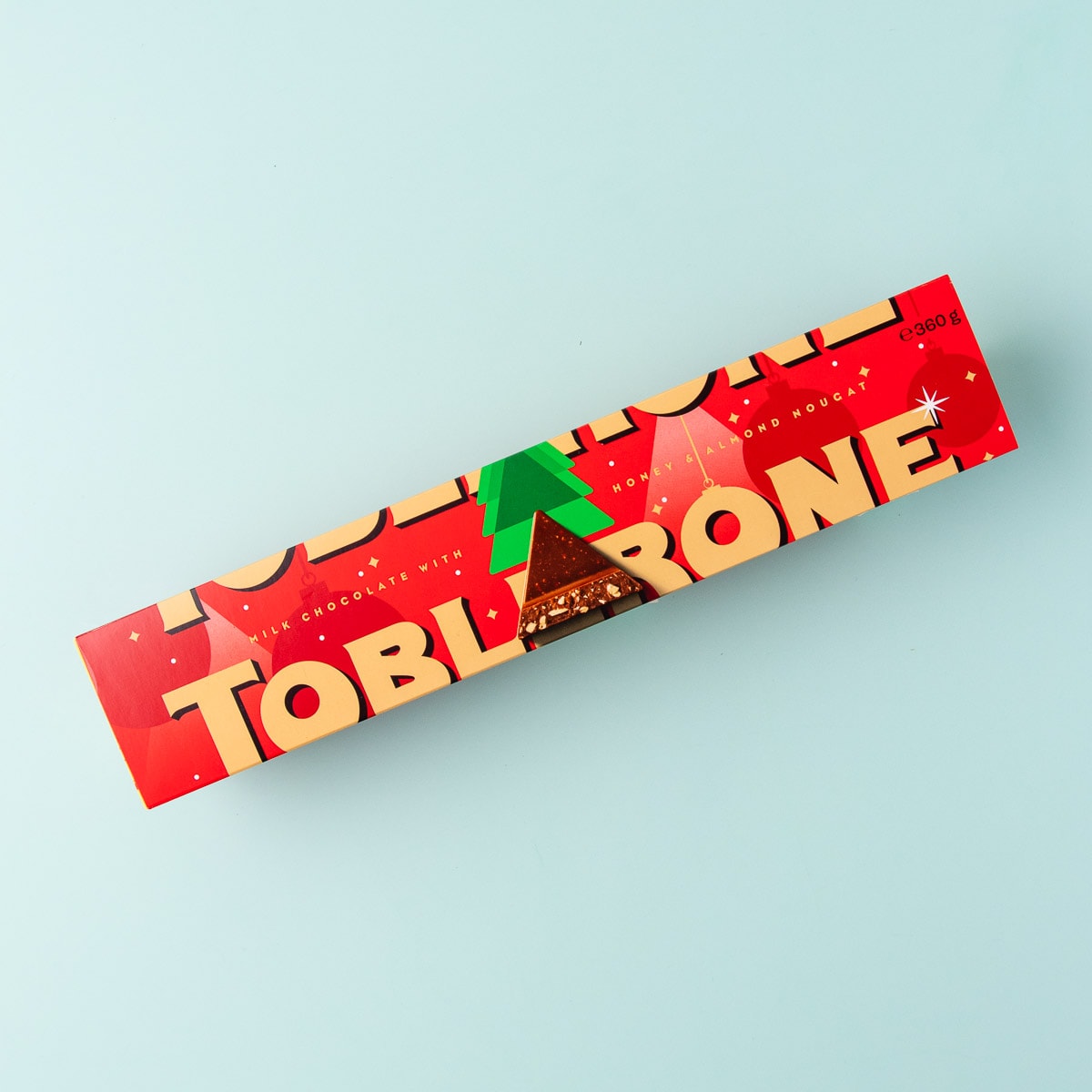 A long triangular block of Toblerone in red Christmas-themed packaging, on a mint green background.