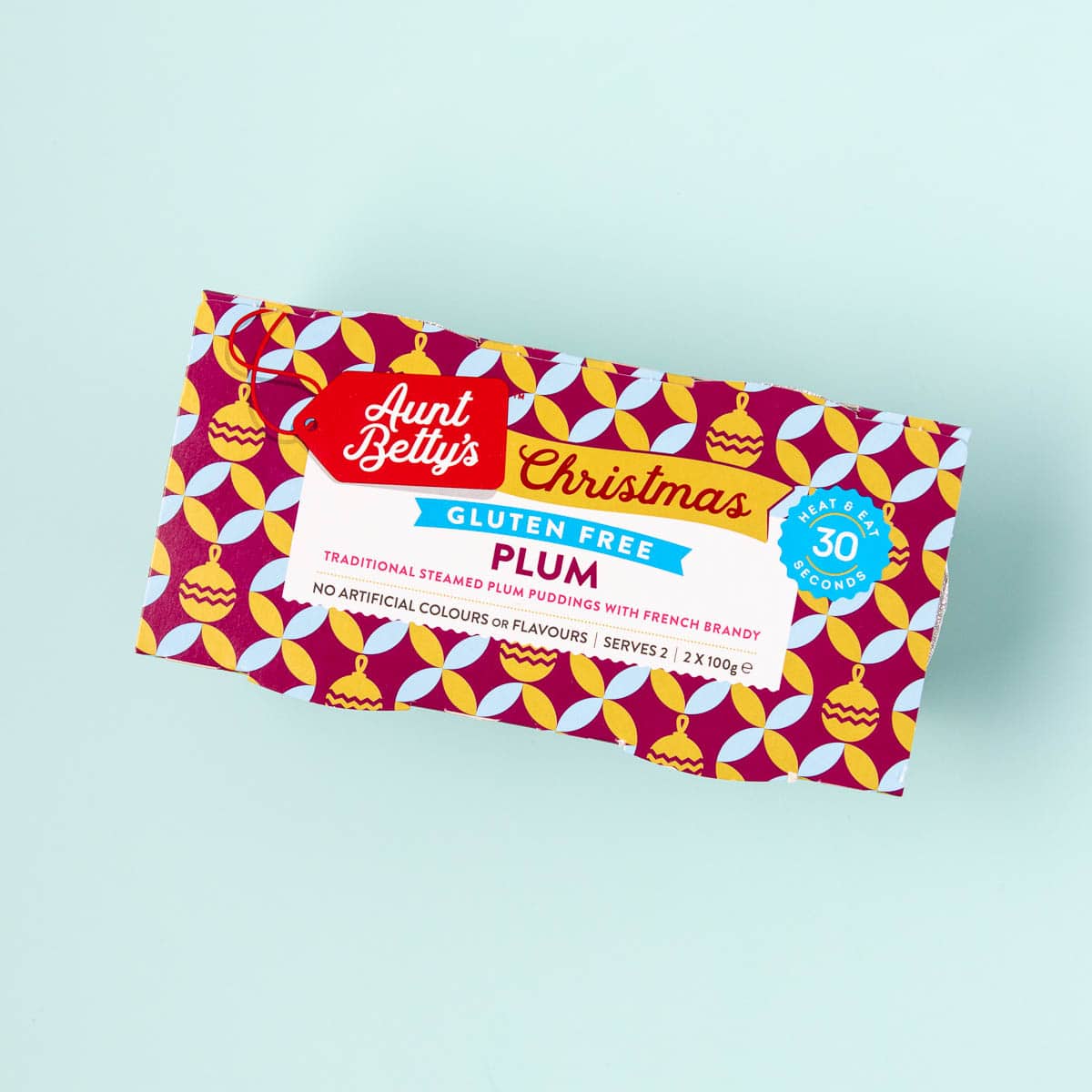 A two-pack of Aunt Betty's gluten free Christmas plum puddings on a mint green background.