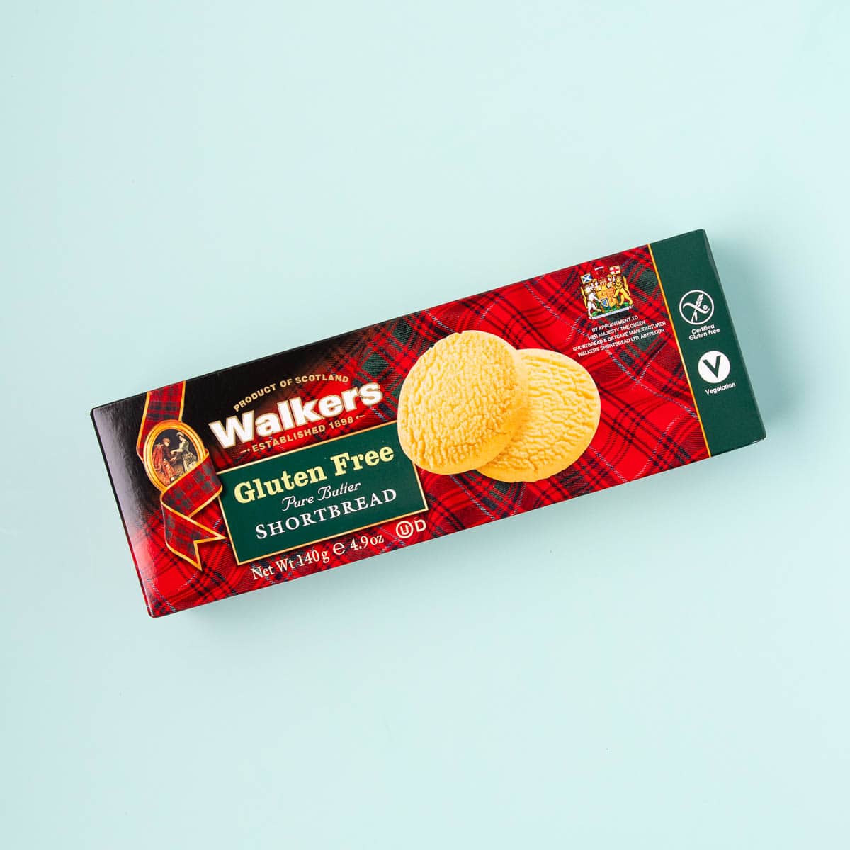 A red tartan-patterned box of Walker's gluten free shortbread on a mint green background.