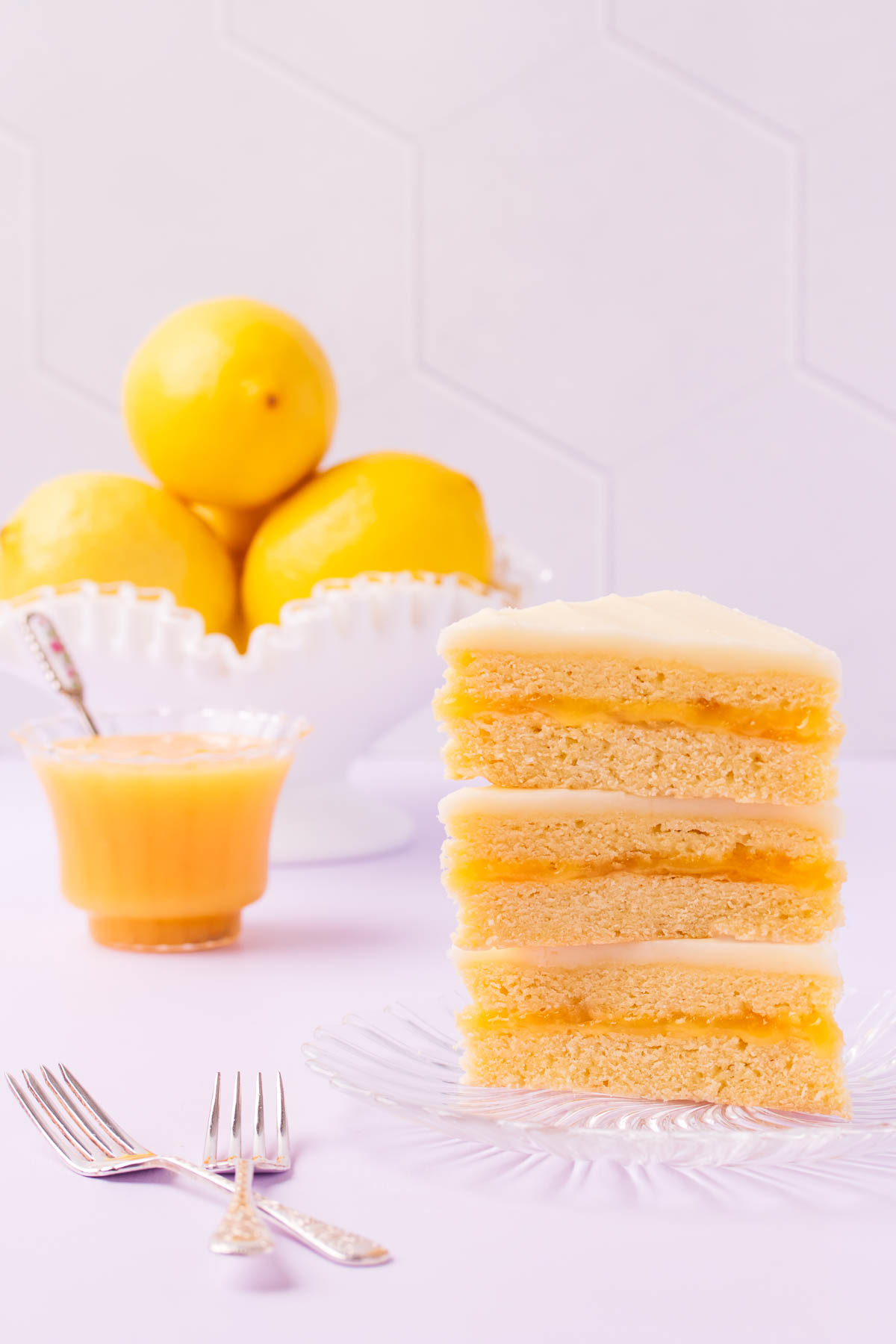 Three triangular pieces of lemon slice stacked on top of each other on a glass plate with a bowl of lemons in the background.