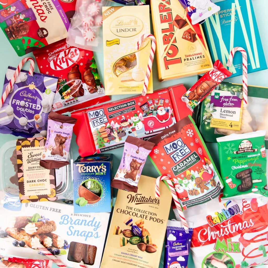 An assortment of gluten free Christmas chocolate and other sweet treats all jumbled together on a mint green background.