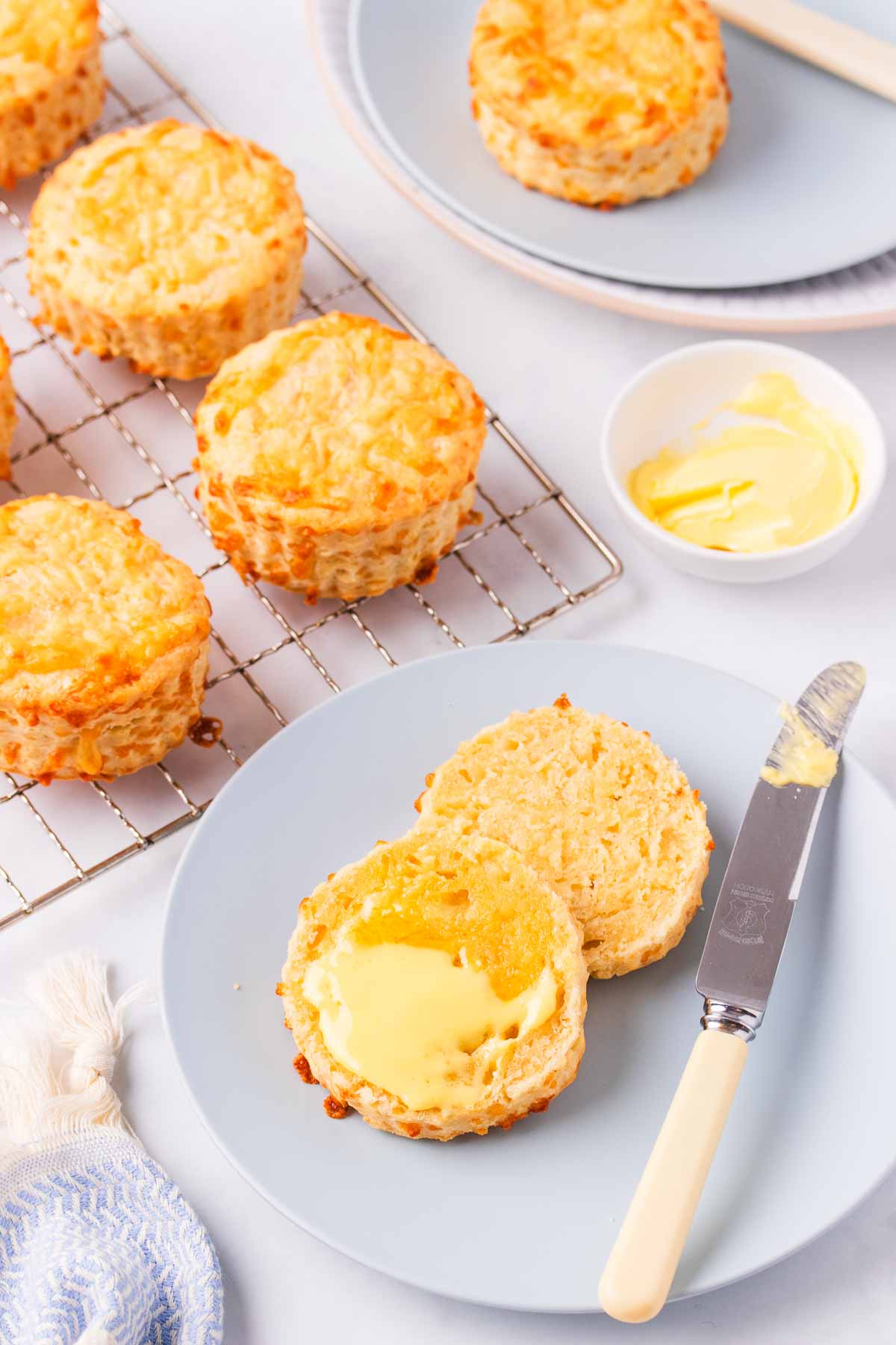 A split cheese scone spread with butter on a light blue plate, with a bone handled knife on the side.