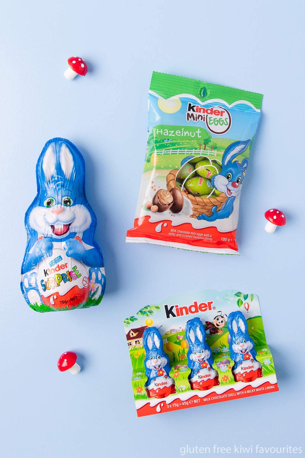 A Kinder Surprise hollow bunny, 3-pack of mini bunnies and packet of hazelnut mini eggs, on a blue background. 