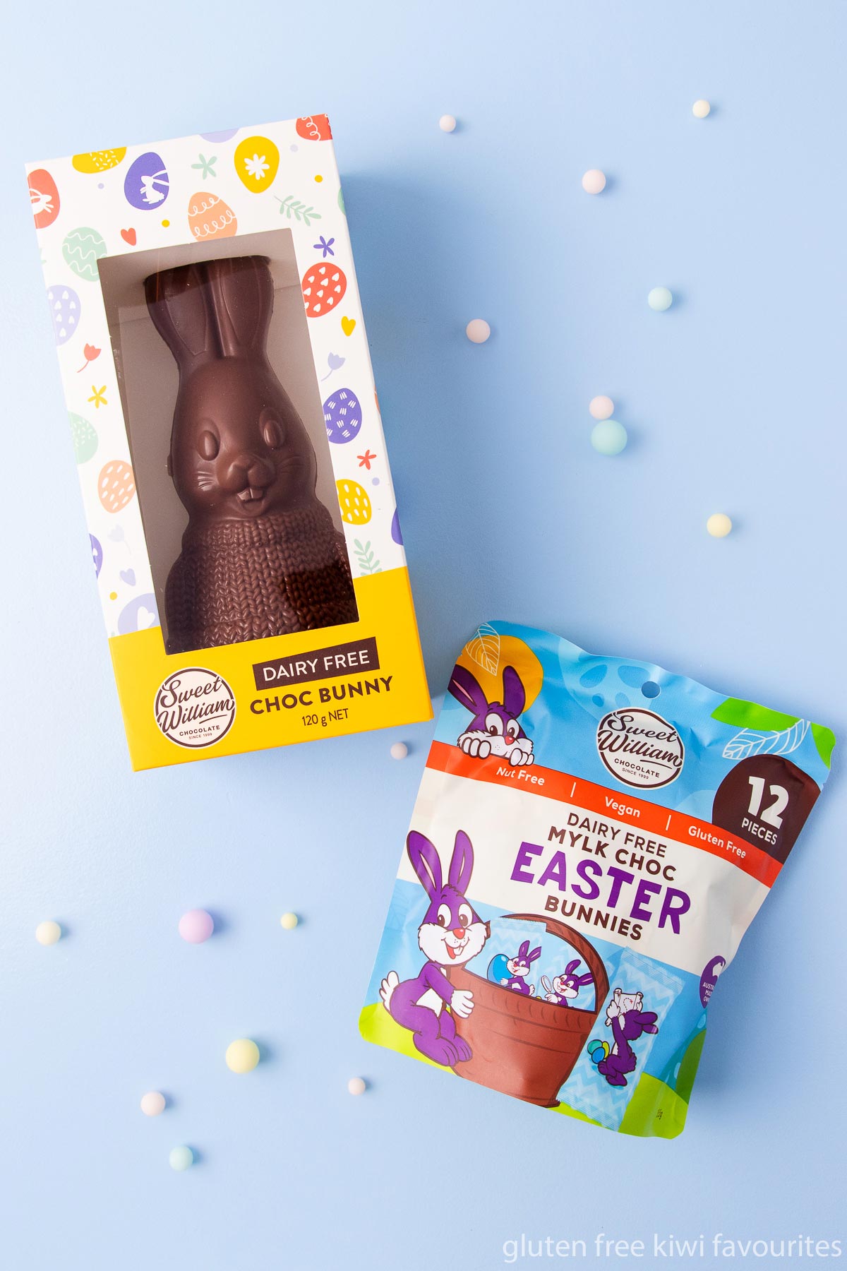 A Sweet William brand dairy free chocolate bunny and packet of mylk choc Easter bunnies on a blue background.
