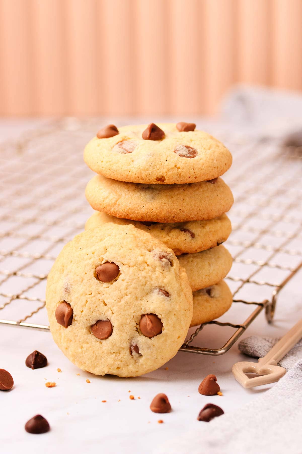 A stack of biscuits on the corner of a rustic metal cooling rack, with scattered biscuit crumbs and chocolate chips.