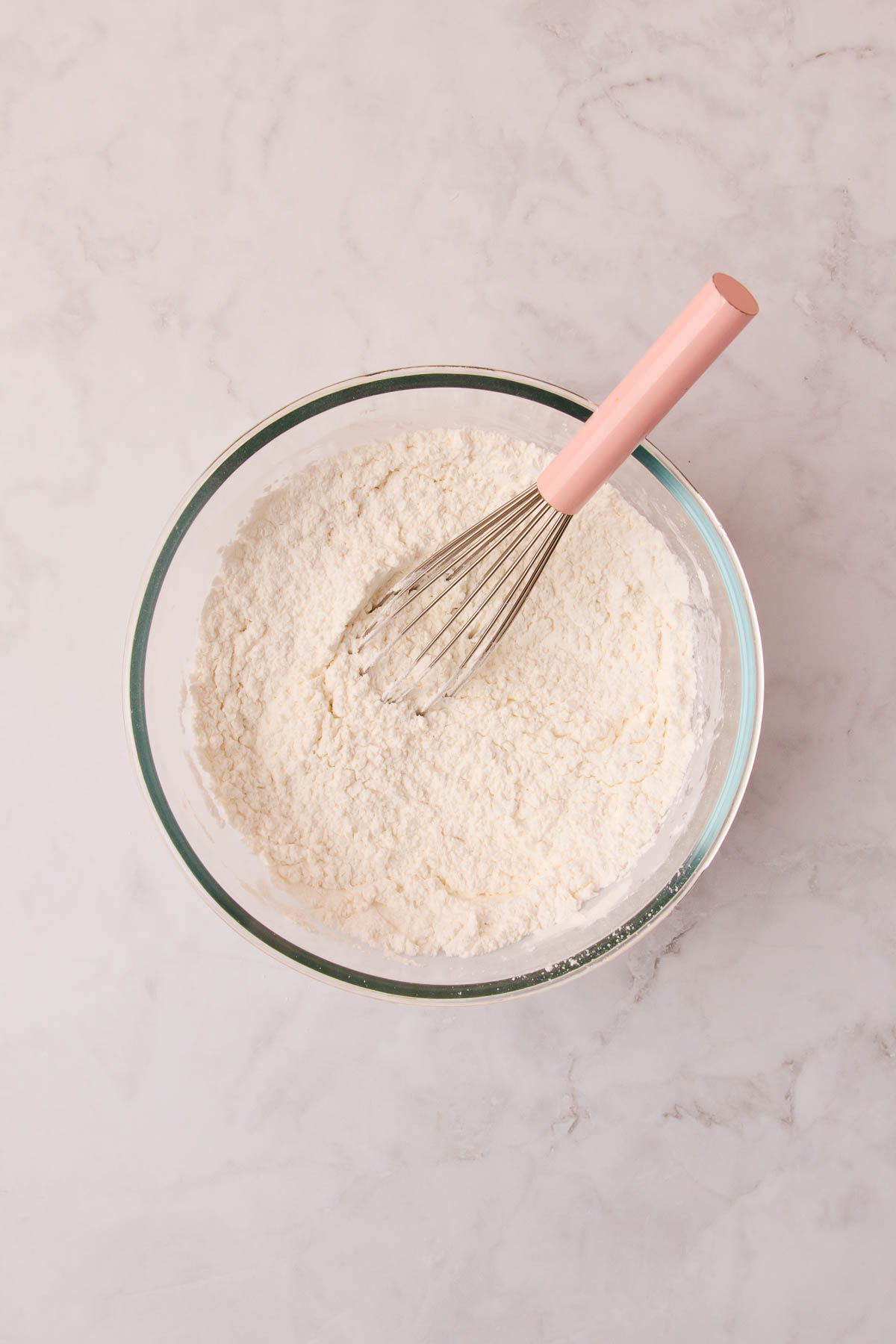 The sifted dry ingredients in a small glass bowl with a pink-handled whisk.