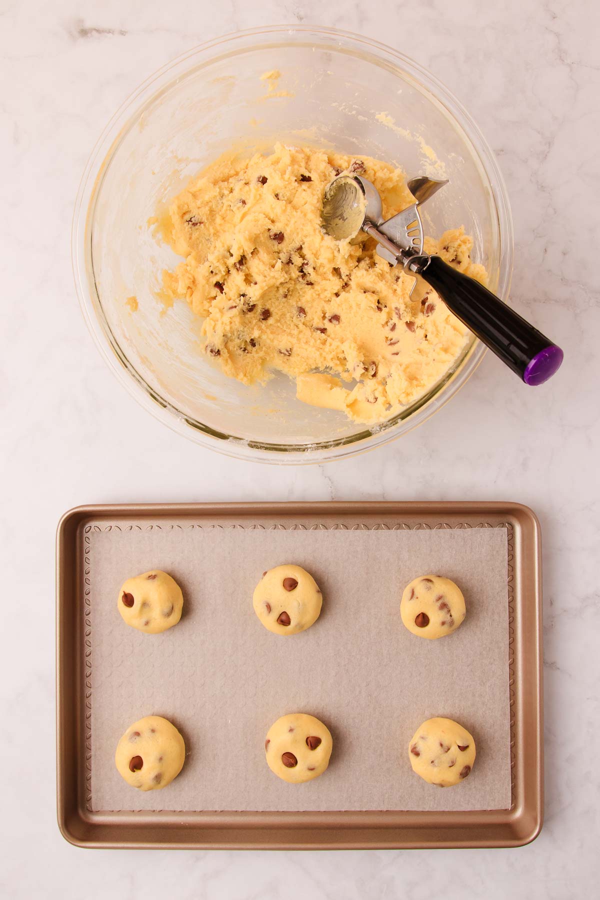 The bowl of biscuit dough, and six balls of the dough on a rose-gold coloured baking tray lined with baking paper. 