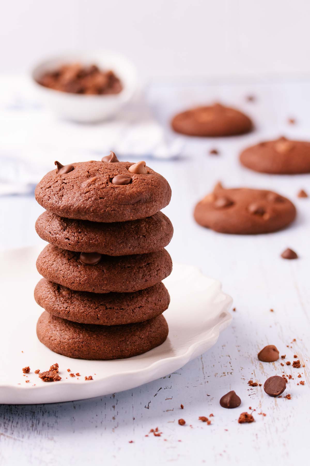 Five chocolate biscuits stacked on a white, scalloped-edge ceramic plate, on a blue-washed wooden background.