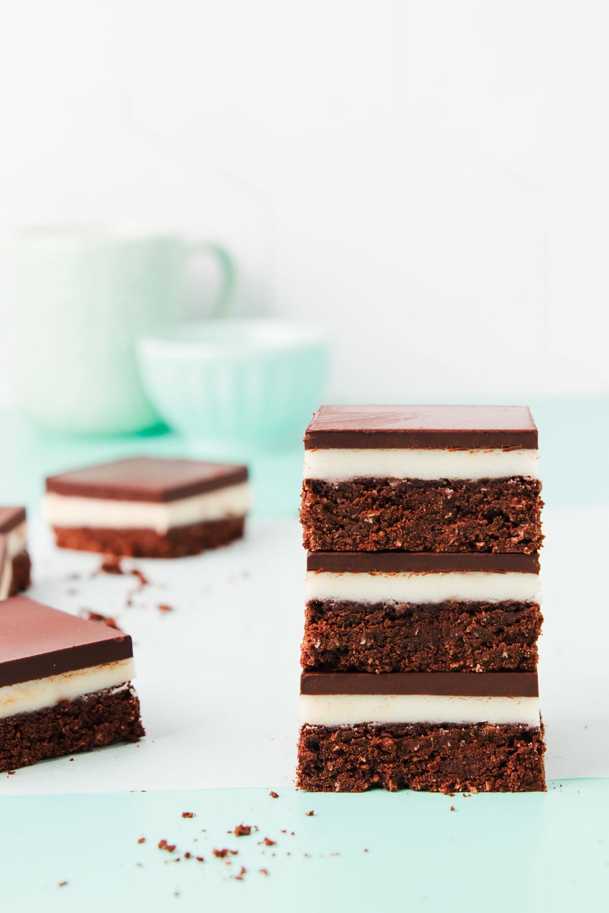 A stack of three square pieces of peppermint slice, on a mint green background.