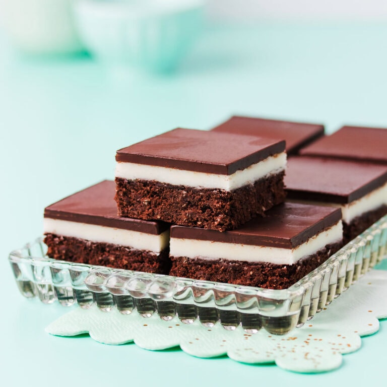 Pieces of gluten-free peppermint slice on a rectangular glass plate, with a mint-green paper napkin on a mint green background.