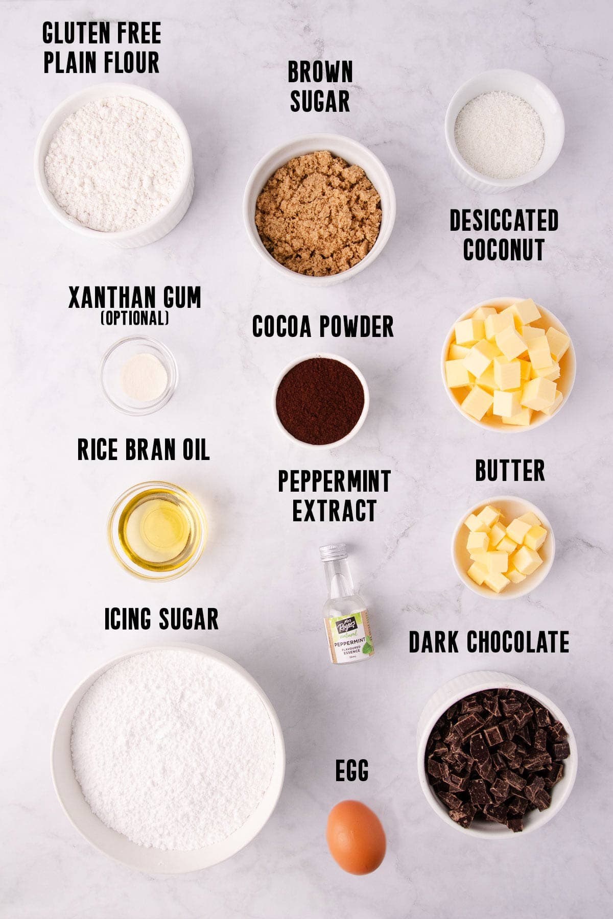 The gluten free peppermint slice ingredients in bowls on a pale grey marble background.