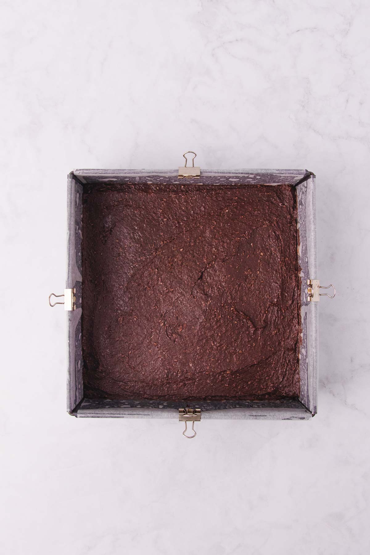 The slice base after being spread into a square cake pan lined with baking paper and secured on the edges with small binder clips.