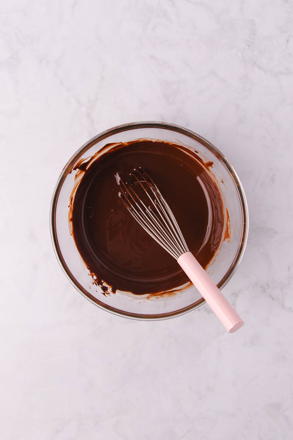 Melted chocolate and oil in a glass bowl with a small hand whisk. 