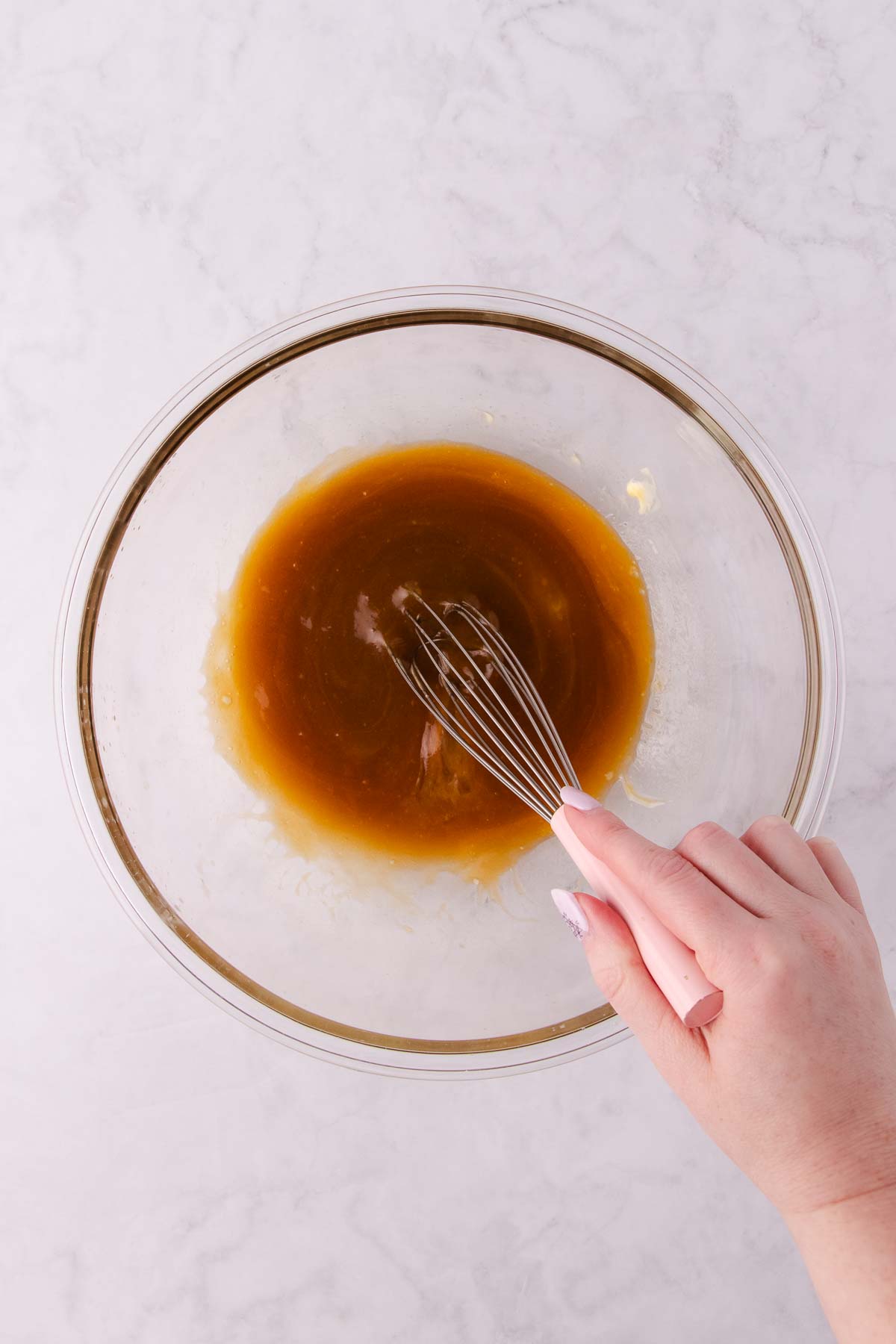 The melted butter, sugar and egg being whisked in a large glass bowl.