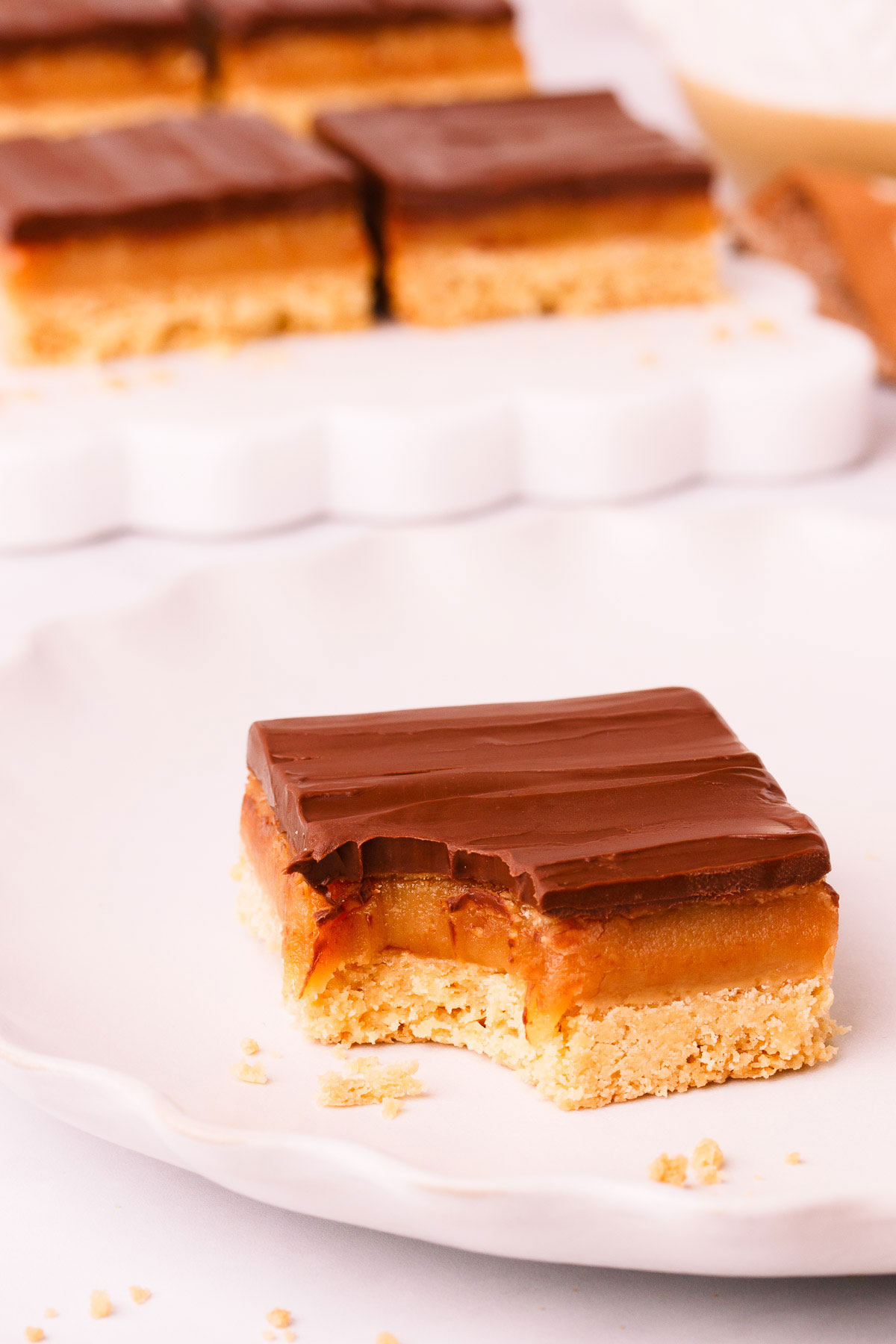 A piece of gluten free caramel slice with a bite taken out of it, on a light grey plate with a scalloped edge.