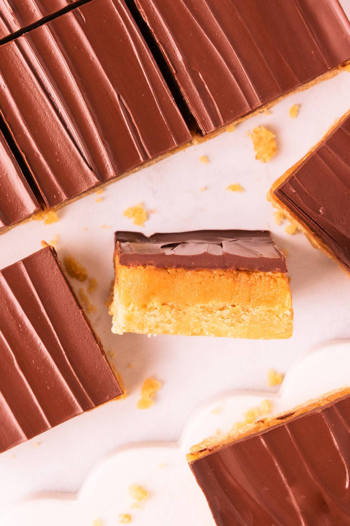 Overhead image of pieces of caramel slice, showing the shiny chocolate topping, with one piece on its side, showing the layers of base, caramel and chocolate topping.