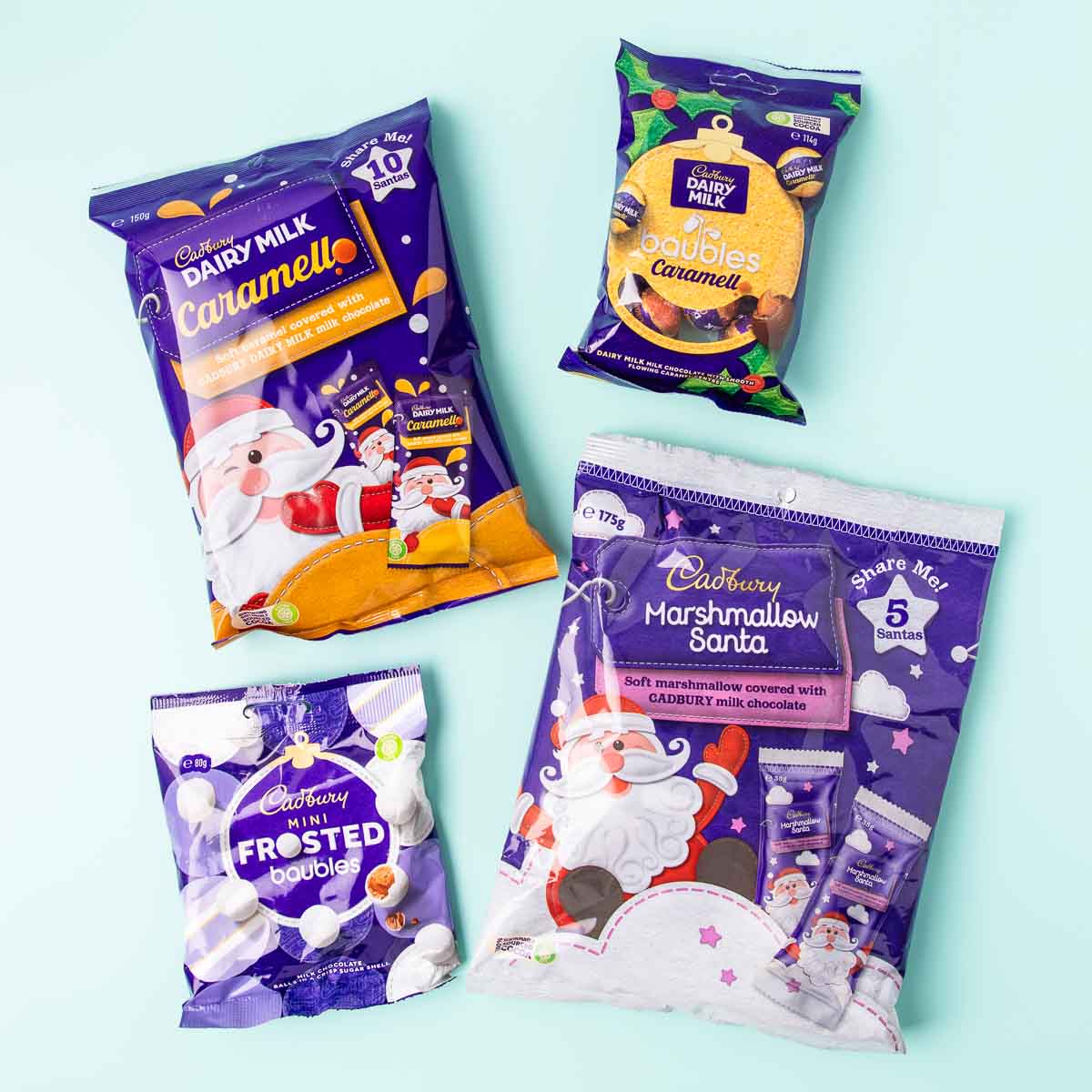 Purple bags of Cadbury marshmallow Santas, Caramello Santas, Caramello Baubles and mini Frosted Baubles, on a mint green background.
