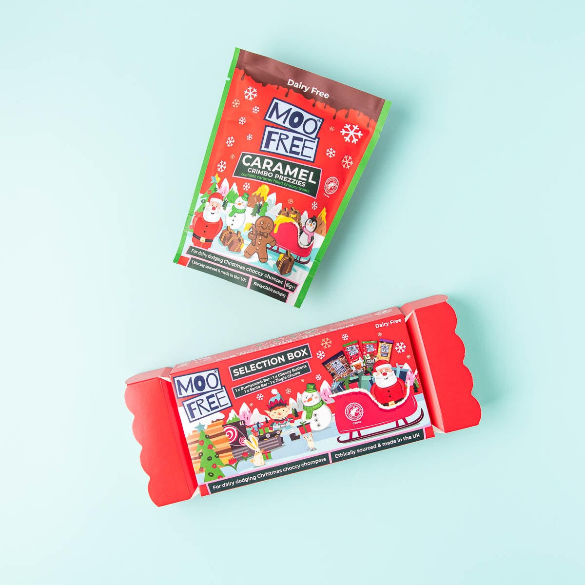 A Moo Free Selection Box which is shaped like a flat Christmas cracker, and a red packet of Moo Free Caramel Crimbo Prezzies on a mint green background.