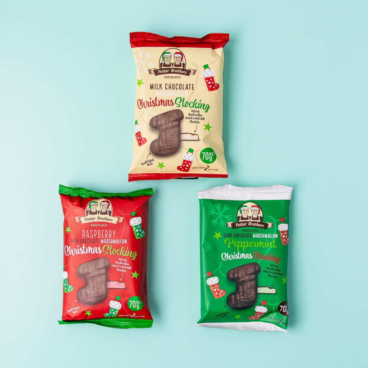 Three Potter Brothers marshmallow stocking packets, one milk chocolate, one peppermint and one raspberry, on a mint green background.