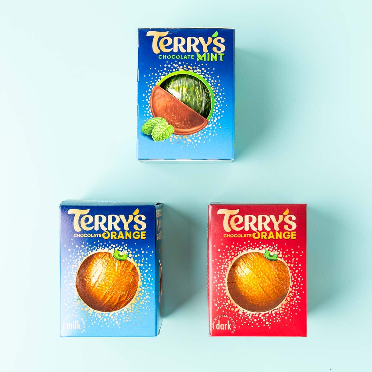 A Terry's dark chocolate orange, milk chocolate orange and chocolate mint, on a mint green background.