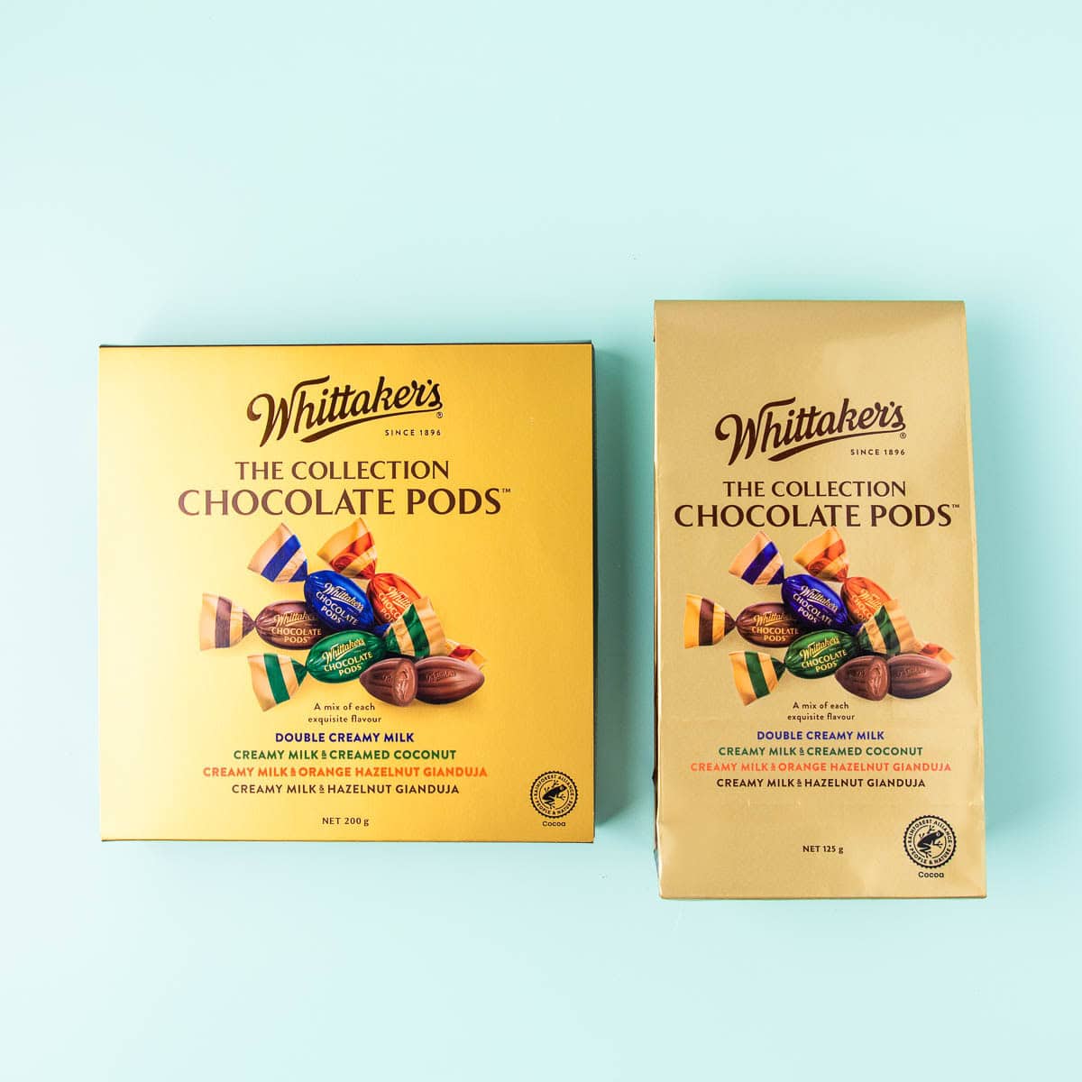 A box and a paper package of Whittakers Chocolate Pods, on a mint green background.