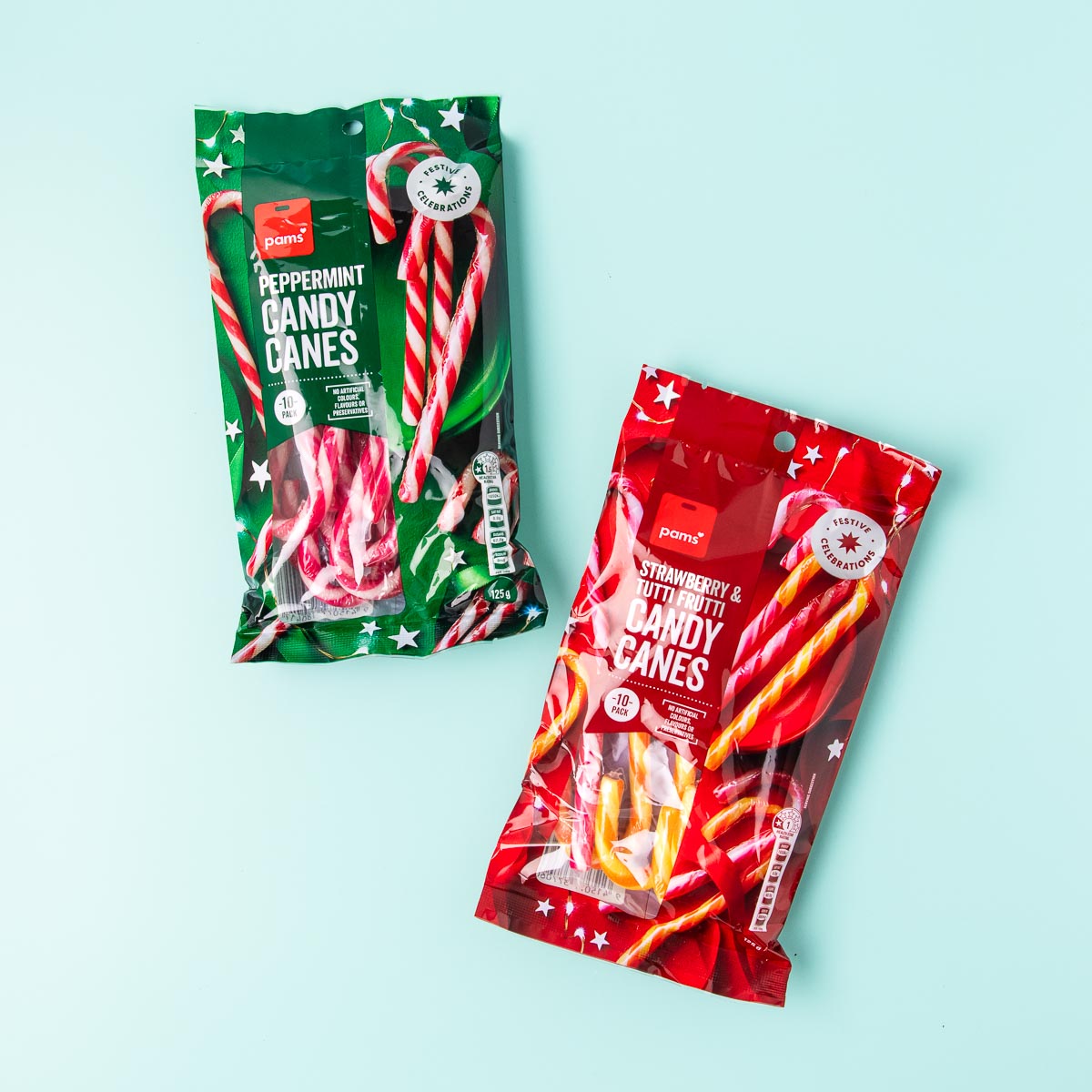 A packet of Pams peppermint candy canes and a packet of strawberry & tutti fruitti candy canes on a mint green background.