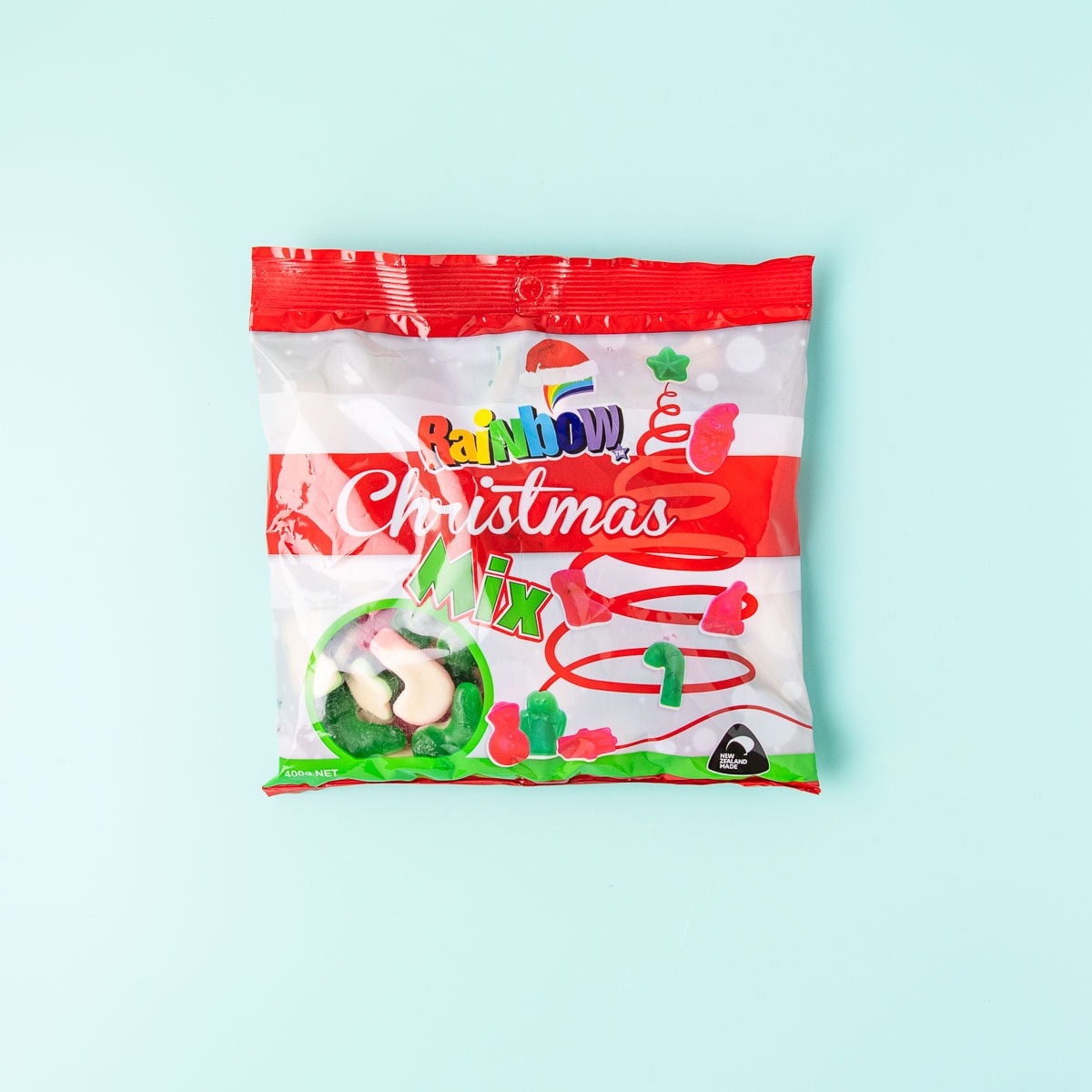 A packet of Rainbow Confectionery Christmas Mix gummy lollies on a mint green background.