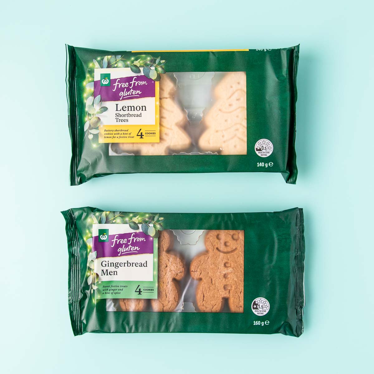 A packet of Free From Gluten Gingerbread Men and one of Lemon Shortbread Trees. The packets are dark green plastic and have a clear window showing the biscuits inside.