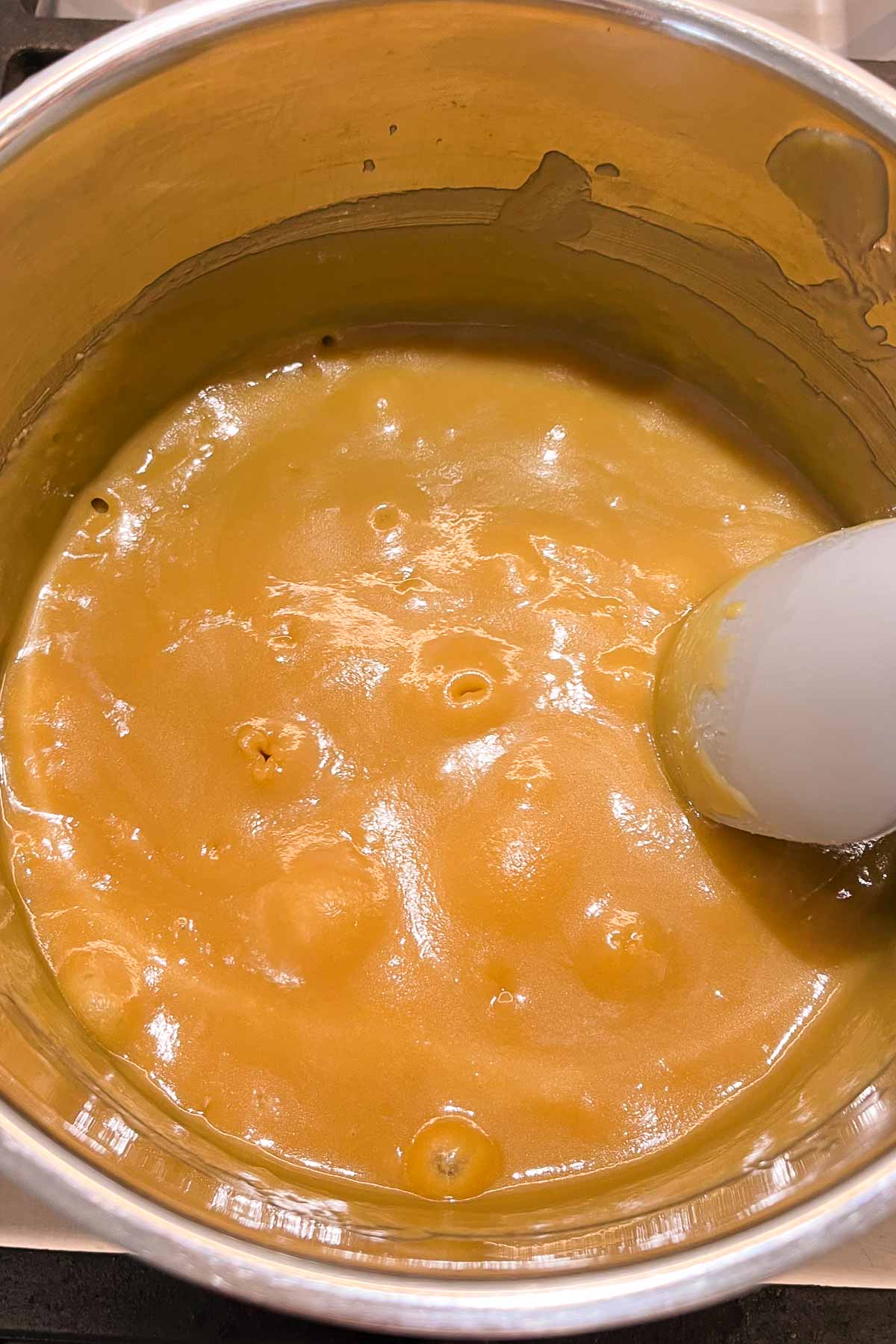 A close up of the caramel being cooked in a stainless steel saucepan, showing the big, slow popping bubbles and the golden colour.