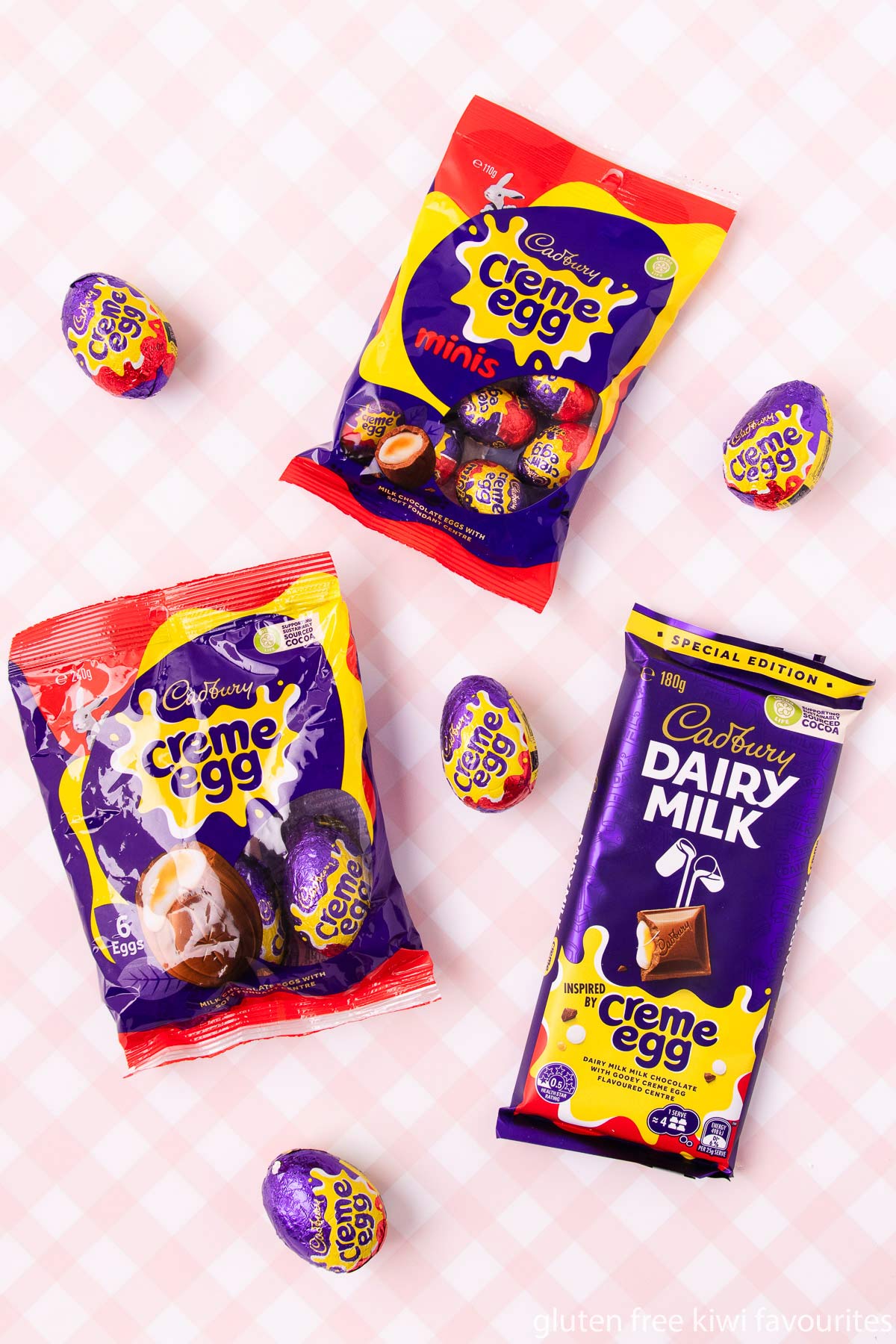 A bag of 40g Cadbury creme eggs, a bag of mini creme eggs, a creme egg chocolate bar and scattered creme eggs, on a pink and white checked background.